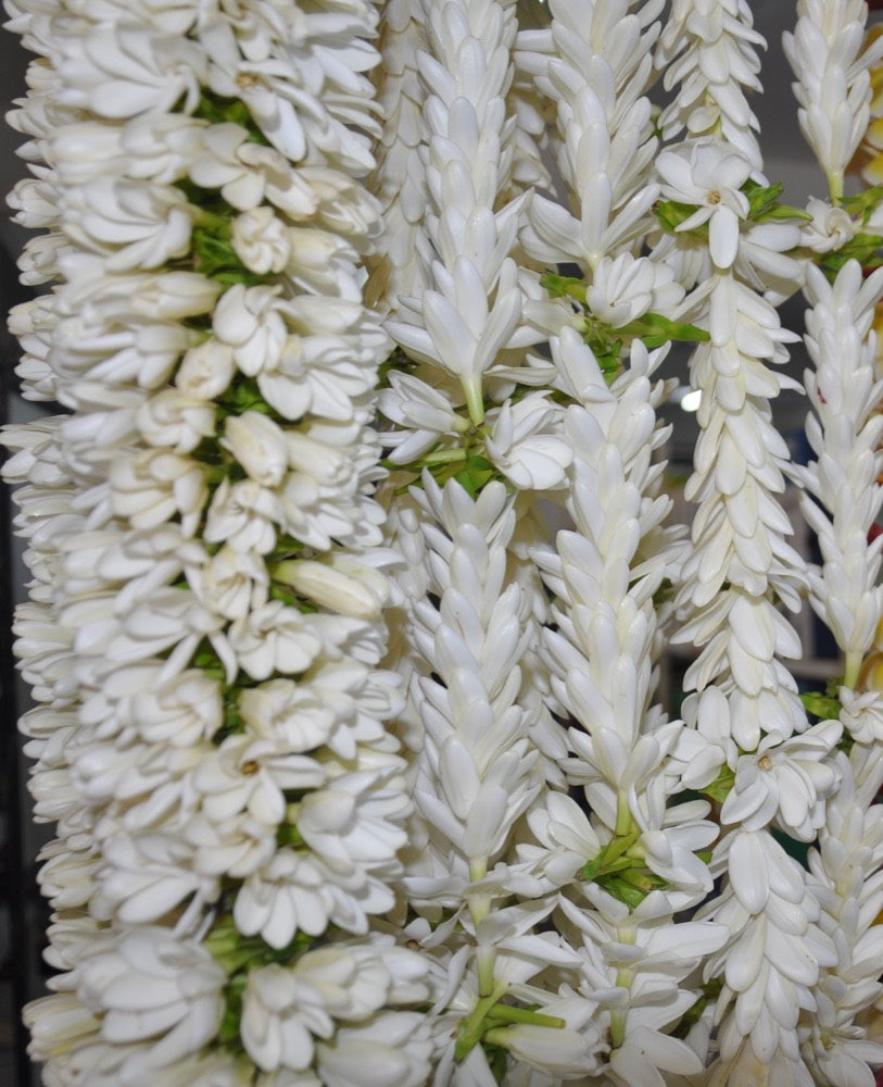 A close-up photograph of garlands made from real tiaré buds and flowers